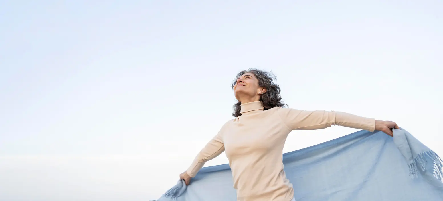 older woman taking a deep breath and running with blanket in open field
