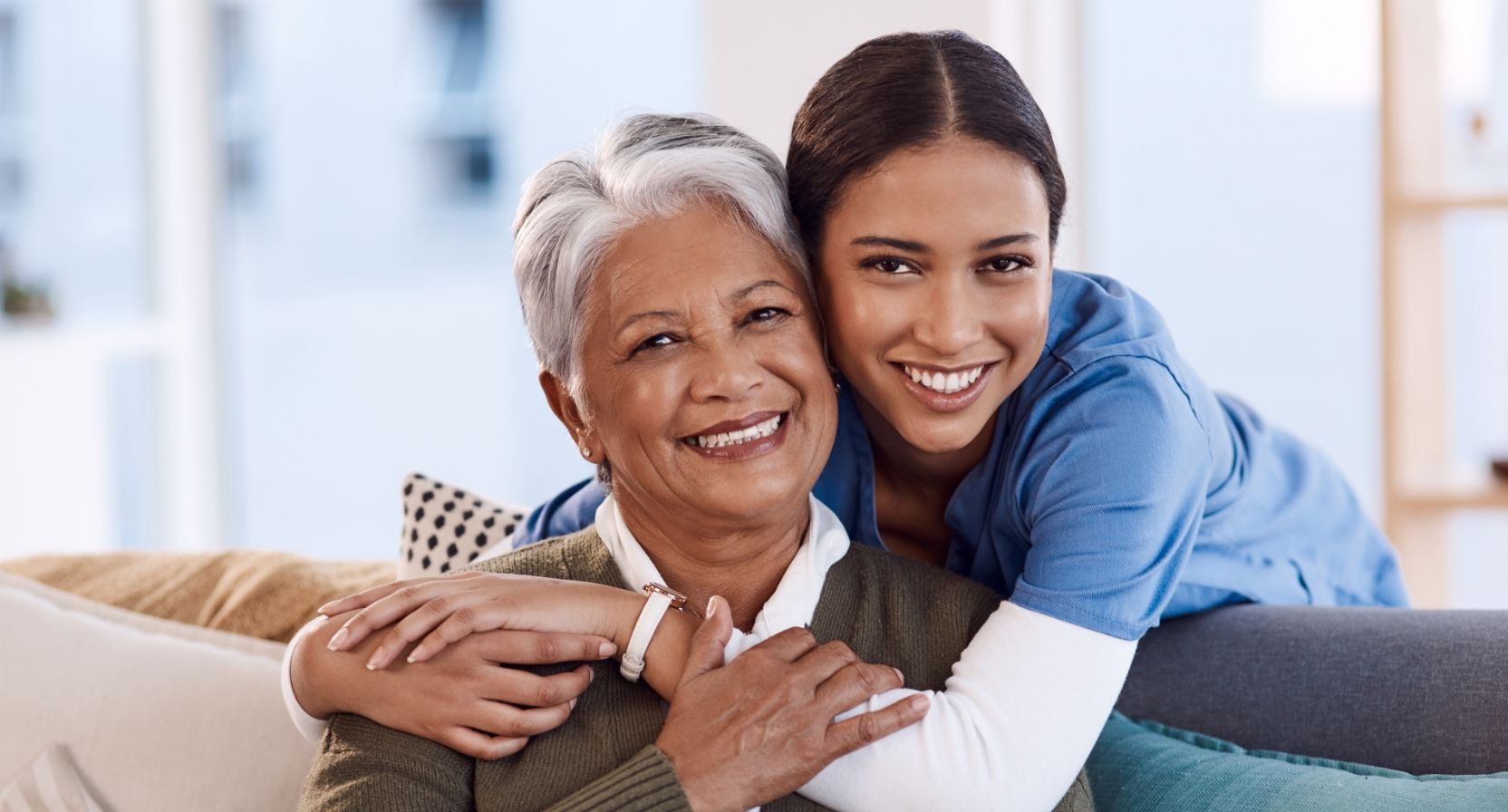 older woman smiling while being hugged by a young woman