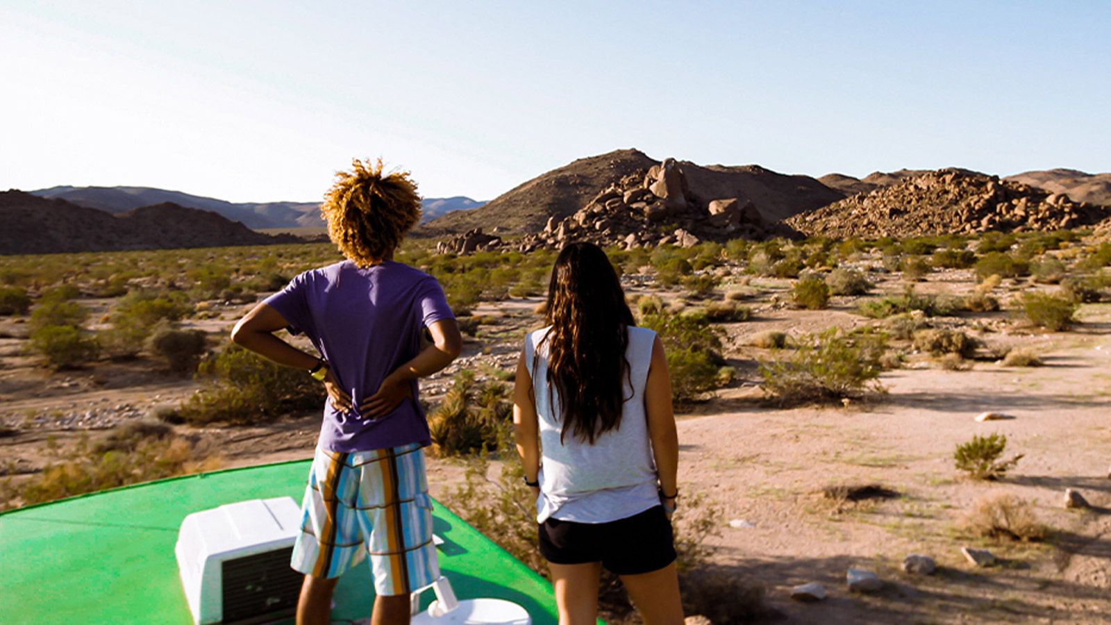 Two young adults look into the distance from the top of the Roadtrip Nation green RV.