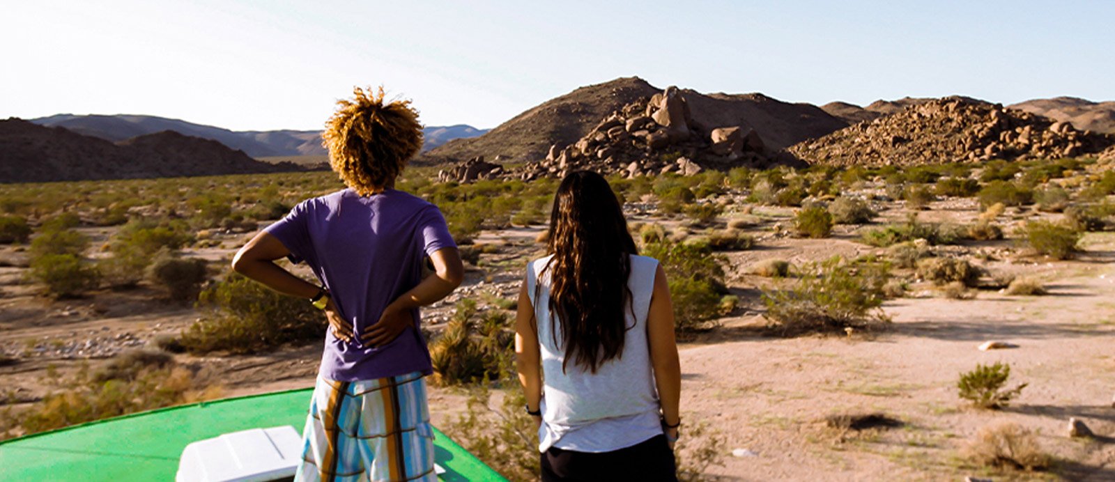 Two young adults look into the distance from the top of the Roadtrip Nation green RV.