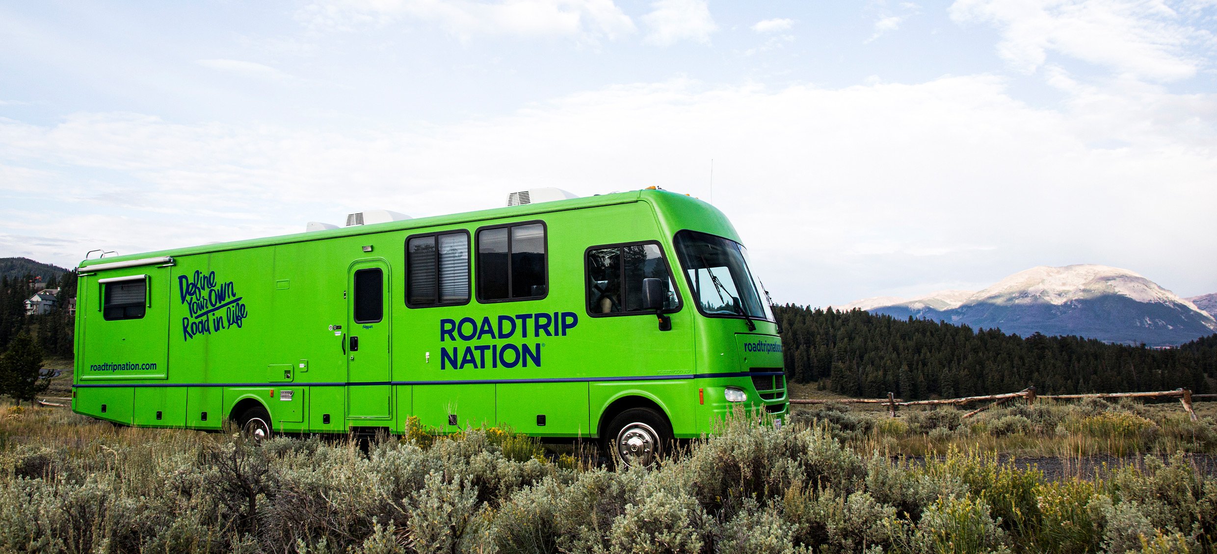 Roadtrip Nation's green RV parked in a field in front of a mountain range.