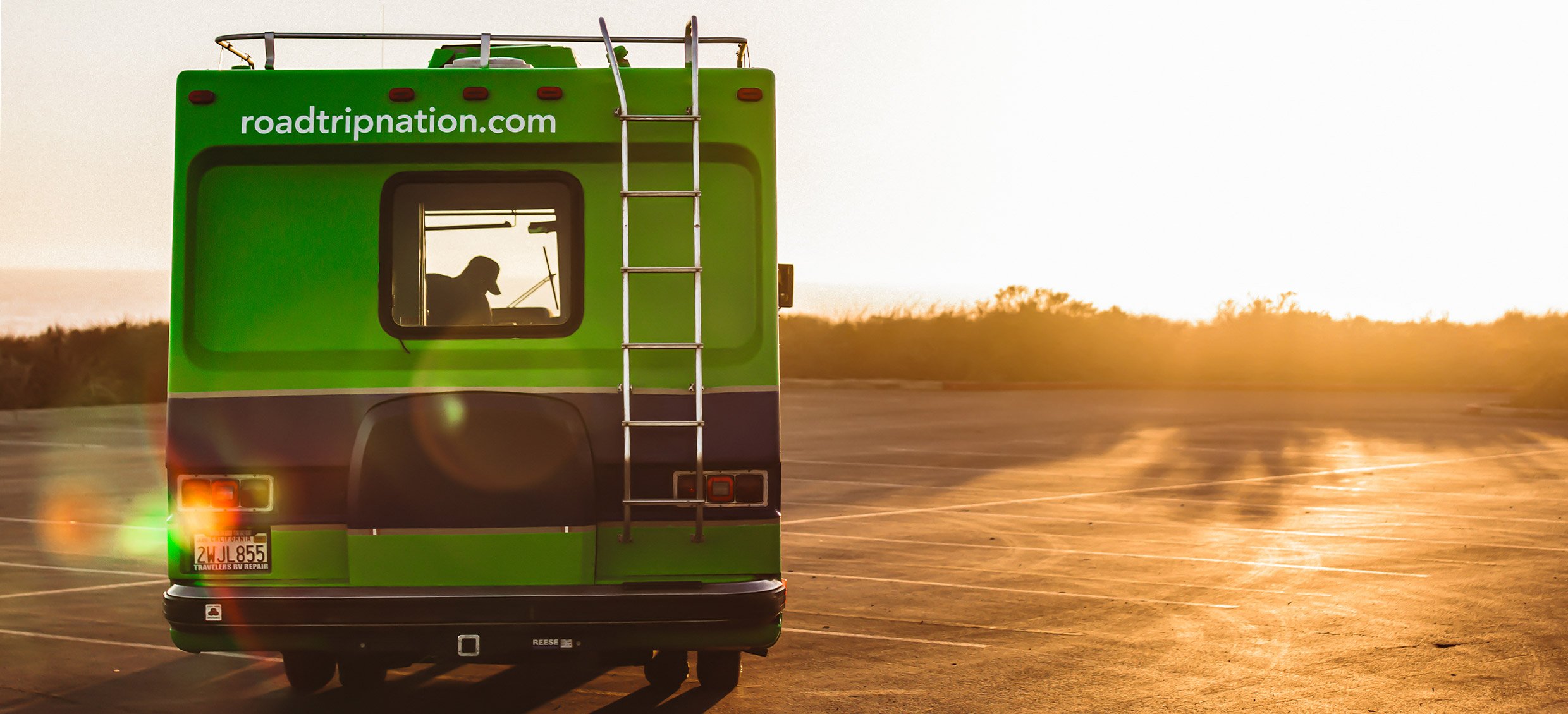 The Roadtrip Nation green RV parked in front of the sunset during golden hour.