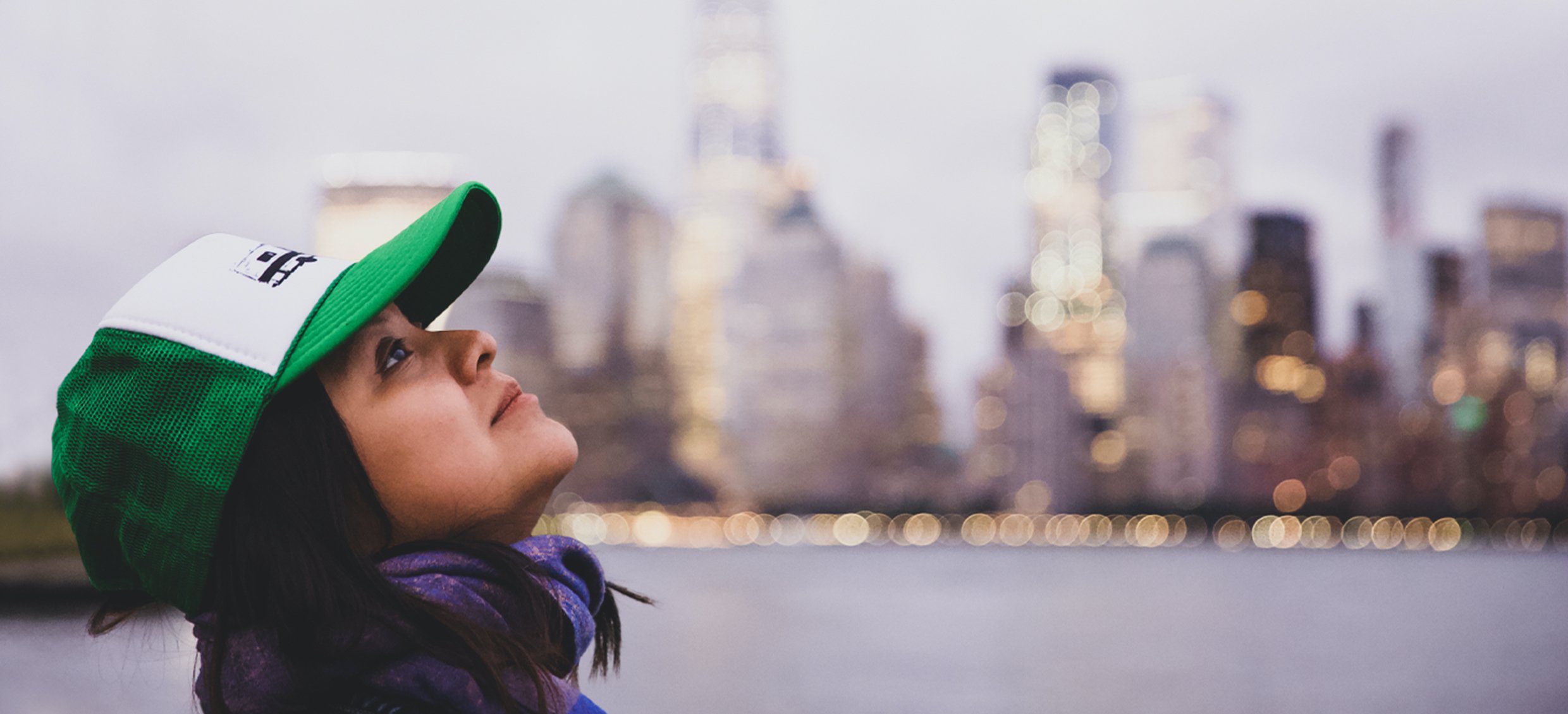 A young woman gazes up hopefully at the sky in front of the New York cityscape.