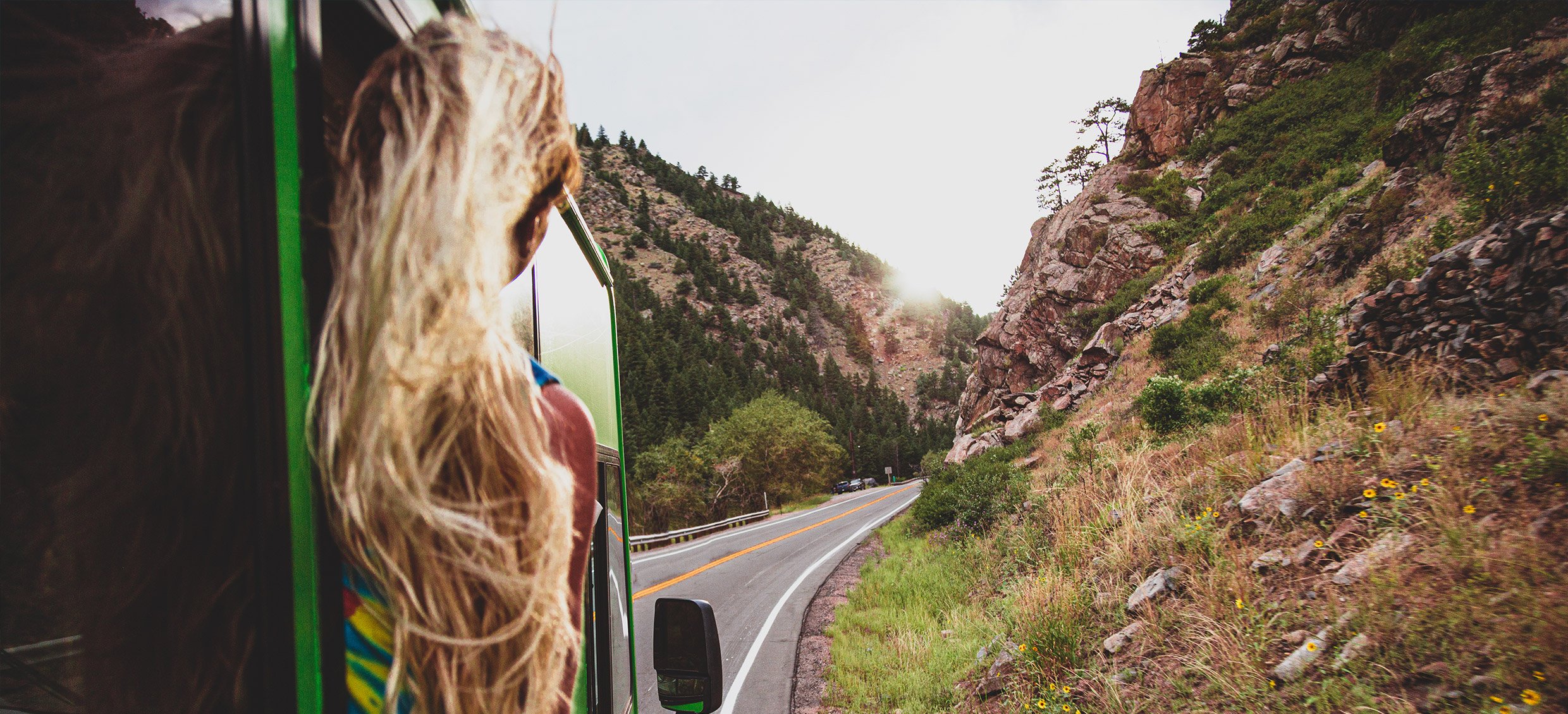 Woman optimistically looks out the window to see the road ahead of the Roadtrip Nation green RV.