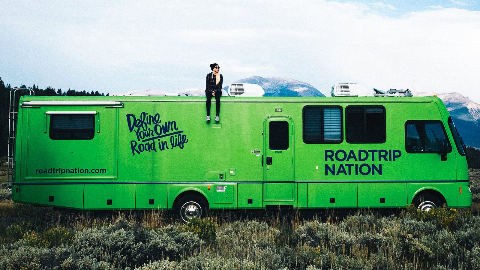 A young woman sits on top of the Roadtrip Nation green RV.