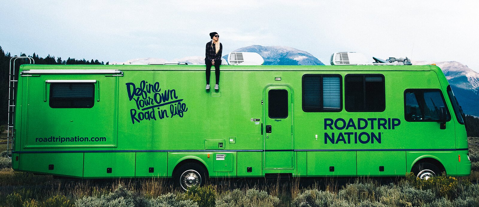 A young woman sits on top of the Roadtrip Nation green RV.