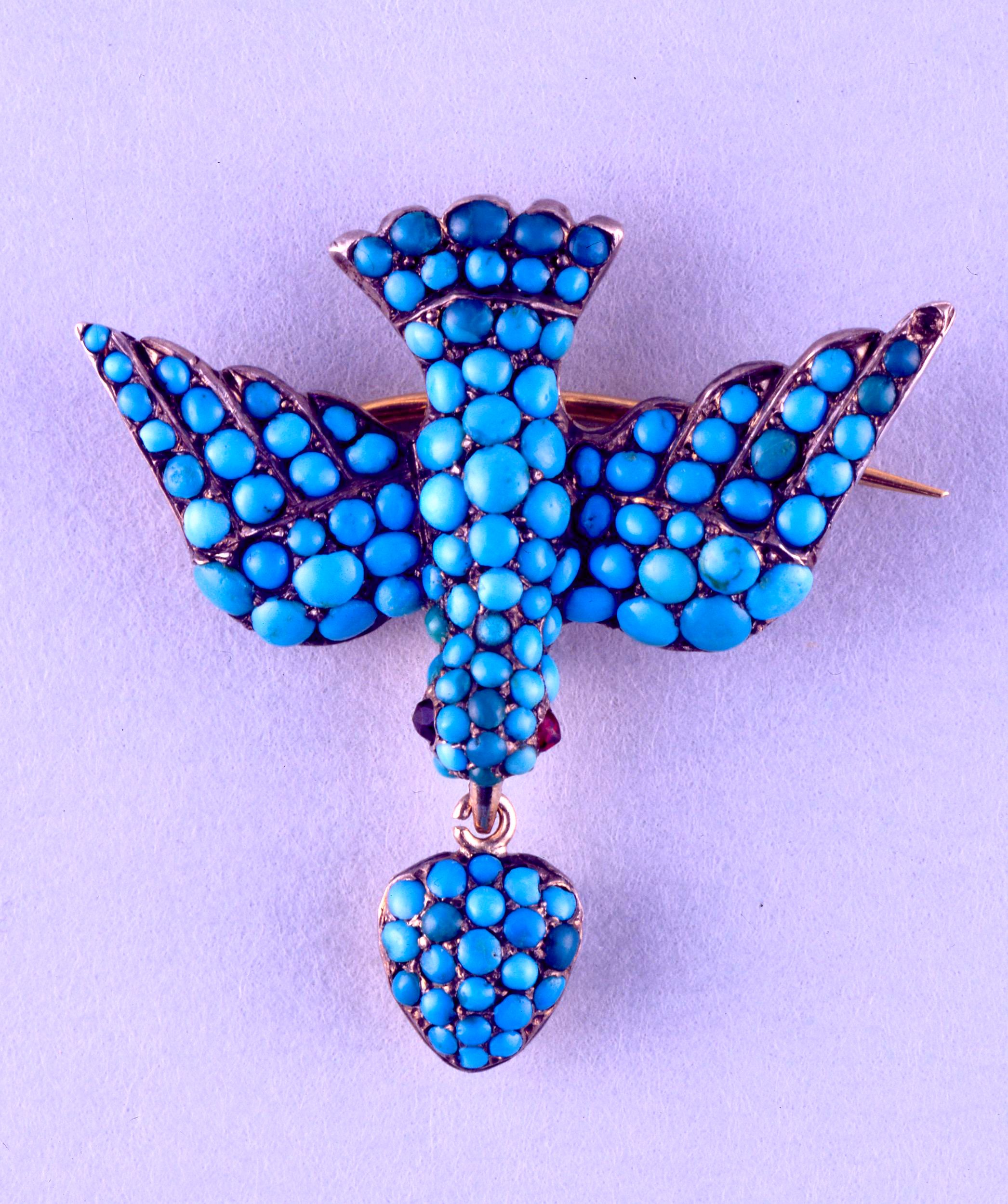 Silver brooch, with a gold backing and pavé-set with turquoises, in the form of a dove with ruby eyes and a pendant heart.