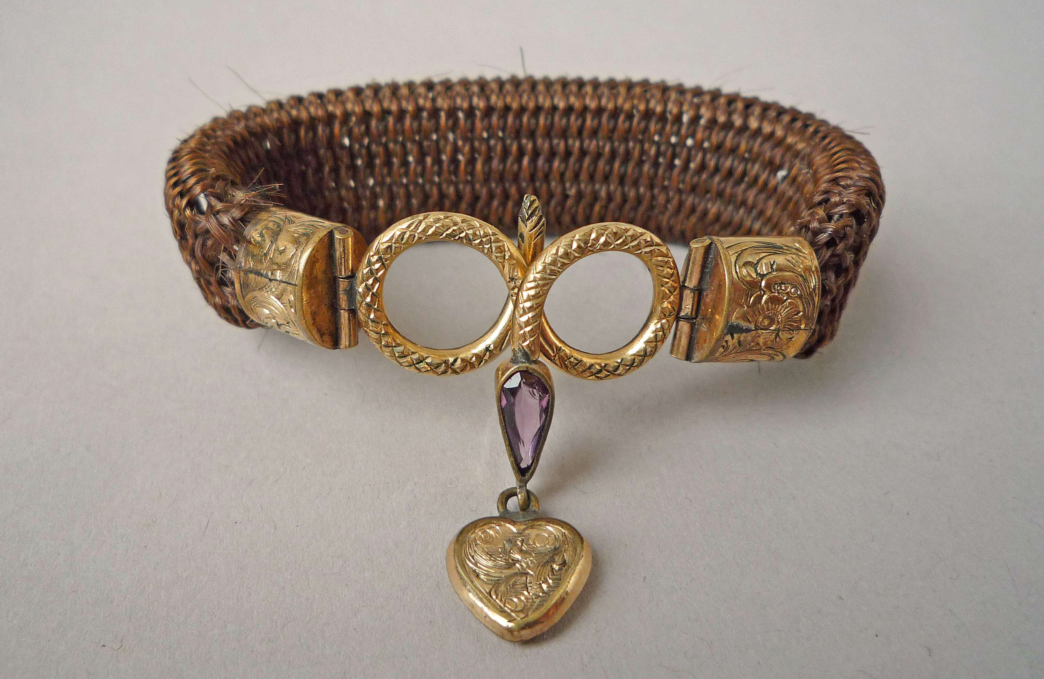 Bracelet of flat plaited hair with engraved gold ends and coiled gold serpent clasp with amethyst drop and small pendant gold heart, thought to be the work of Antoni Forrer, c1850-1870, British Museum