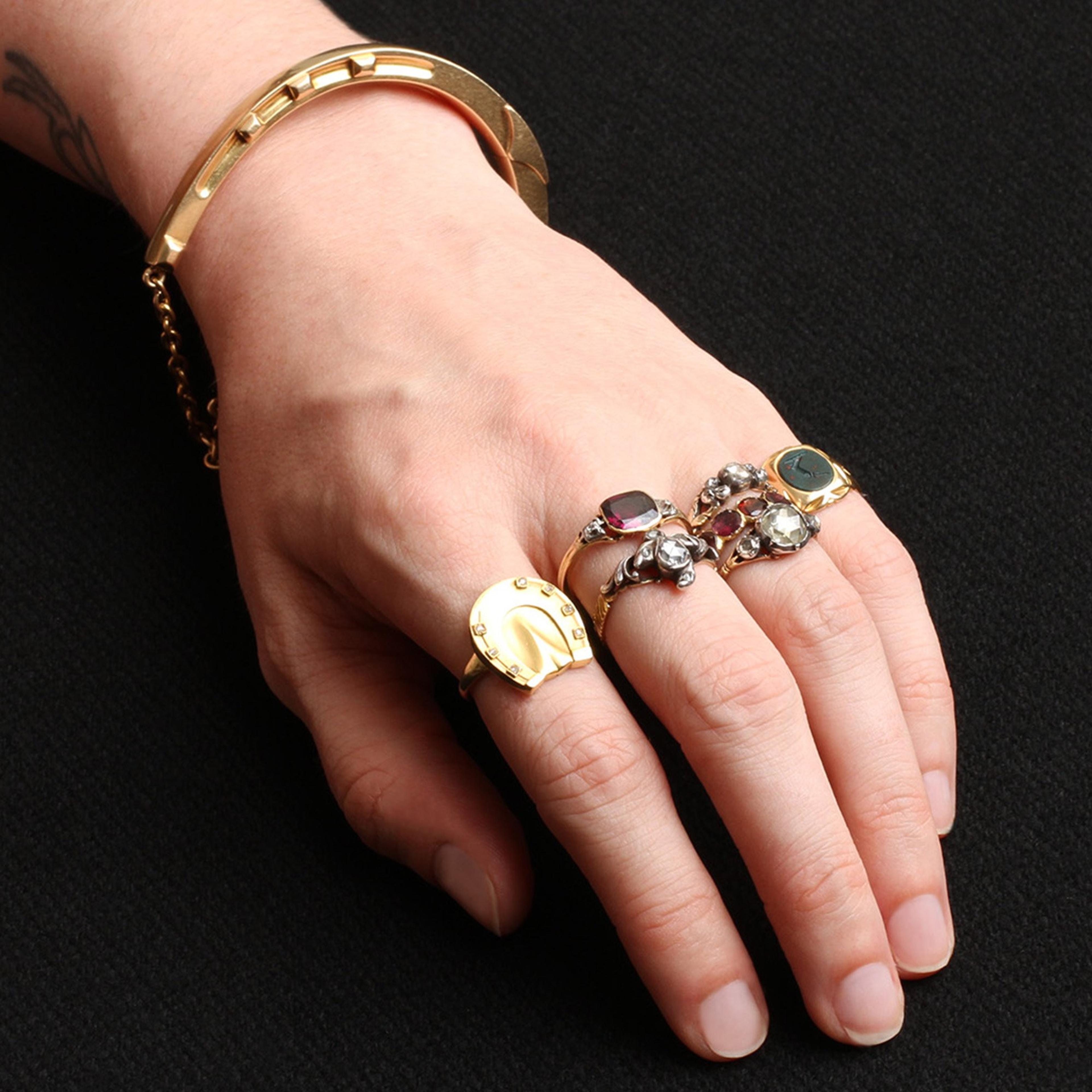 A hand wearing many rings including the Victorian Gold Horseshoe Bangle