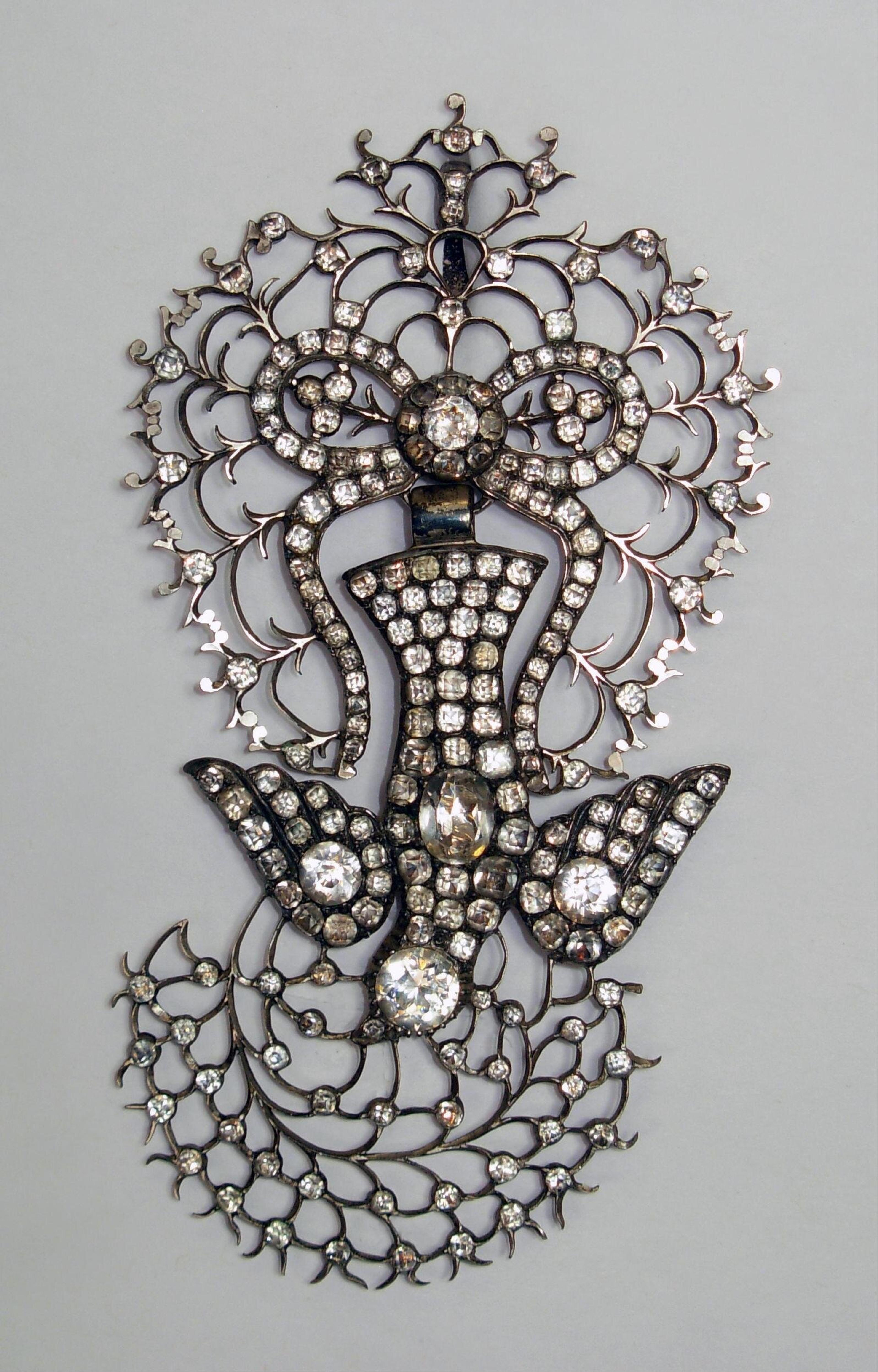 A Saint-Esprit pendant. The dove, symbol of the Holy Spirit (Saint Esprit), flying down to earth with an olive branch. Made in silver set, with clear pastes, 1860-1870. The Victoria & Albert Museum.