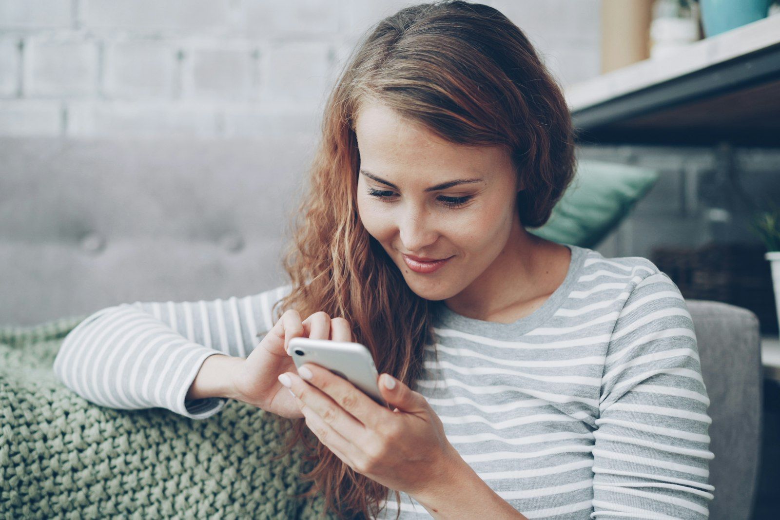 A woman smiling as she uses her phone at home