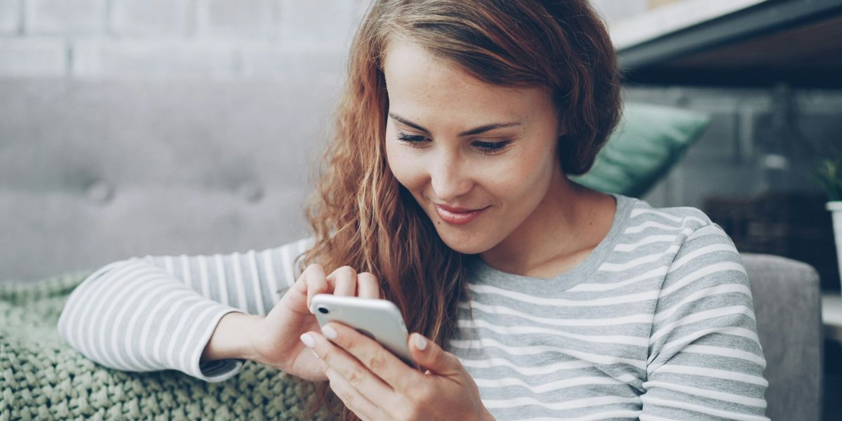 A woman smiling as she uses her phone at home