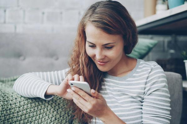 A woman smiling as she uses her phone at home