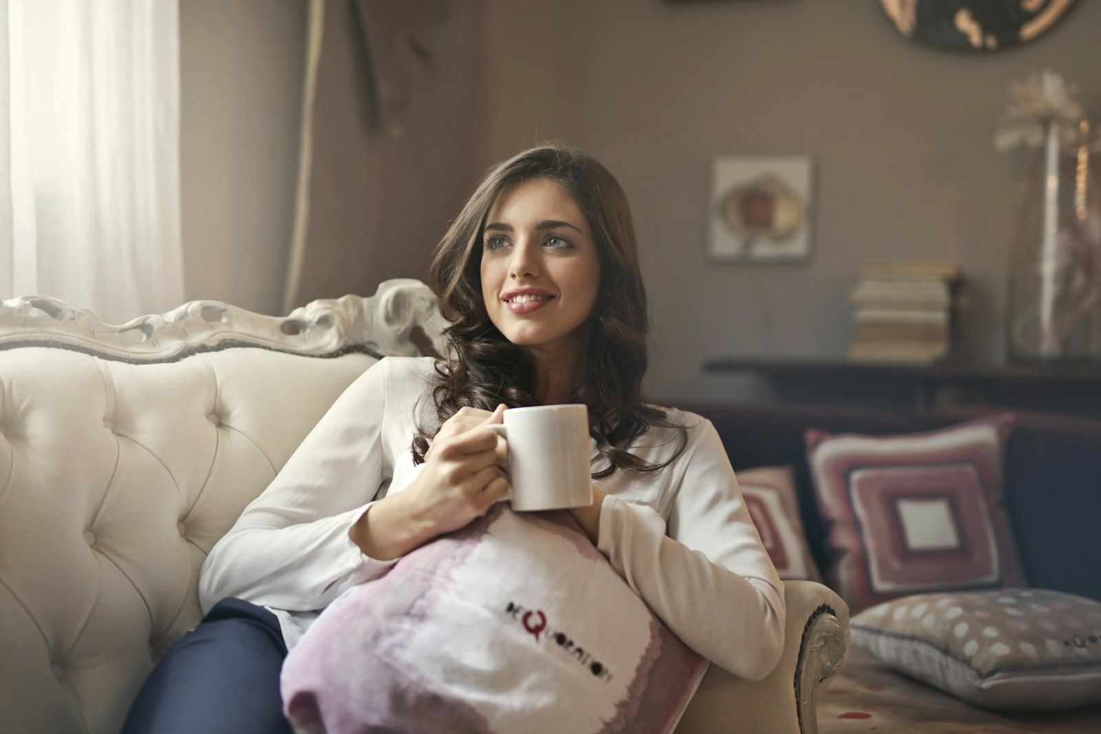 A woman holding a warm drink on her sofa at home