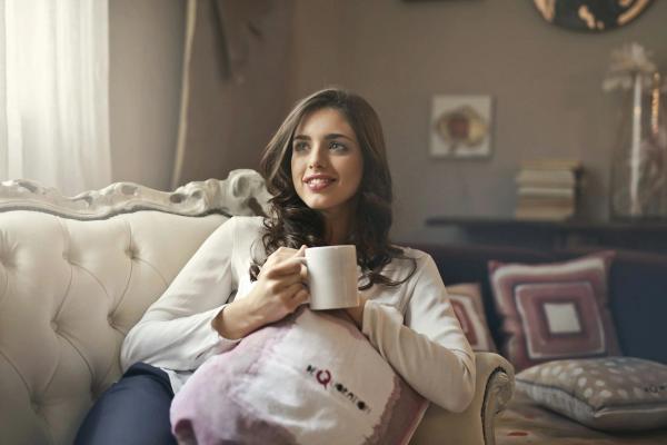 A woman holding a warm drink on her sofa at home
