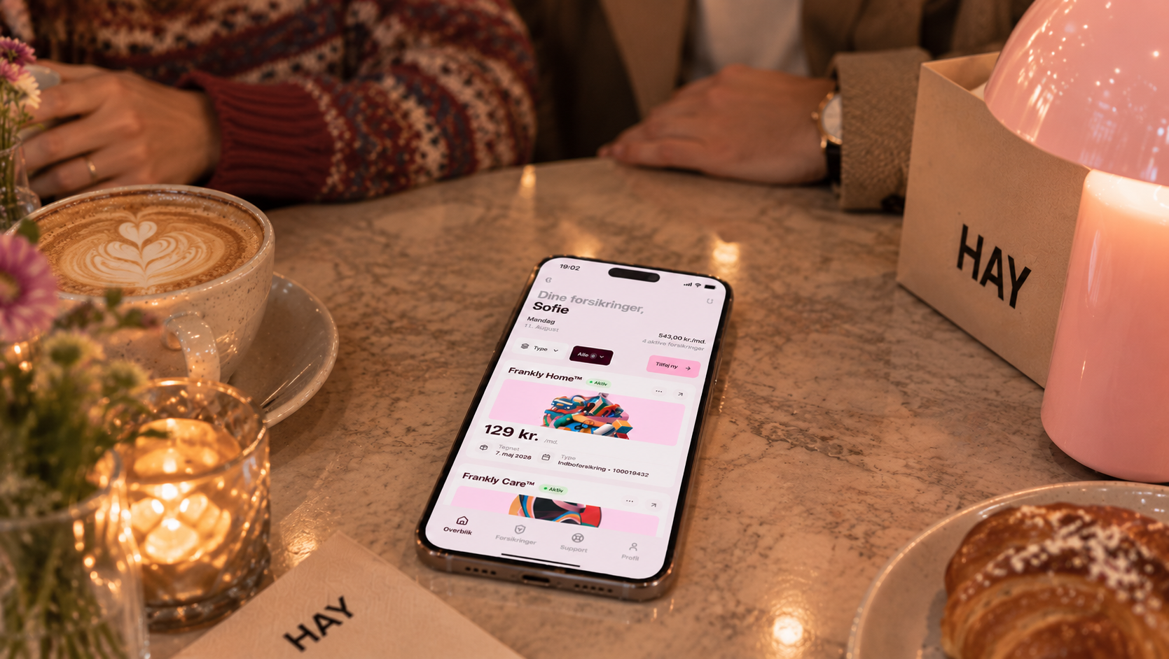 Telefon på cafébordet viser alle forsikringerne samlet ét sted