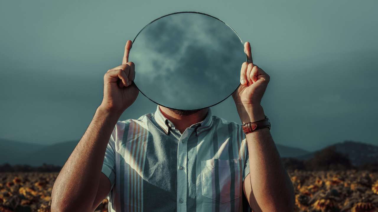 A person holding the mirror facing the camera with wilderness behind