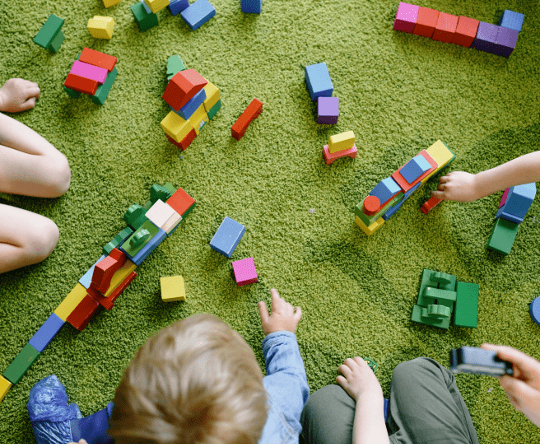 Dzieci bawią się klockami na zielonej macie