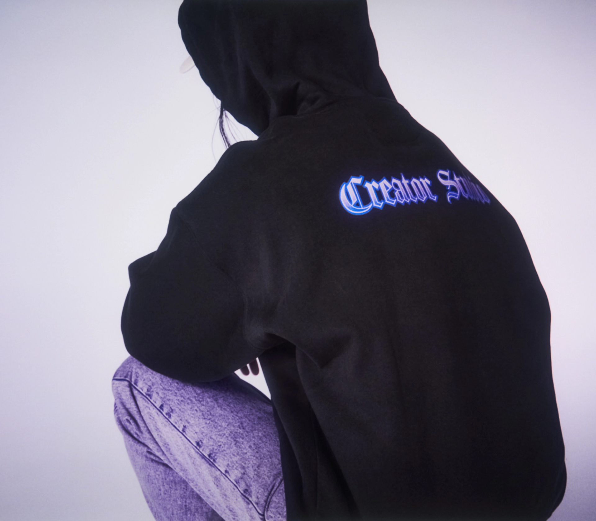 A model wearing a black hoodie with Creator Studio print on the back