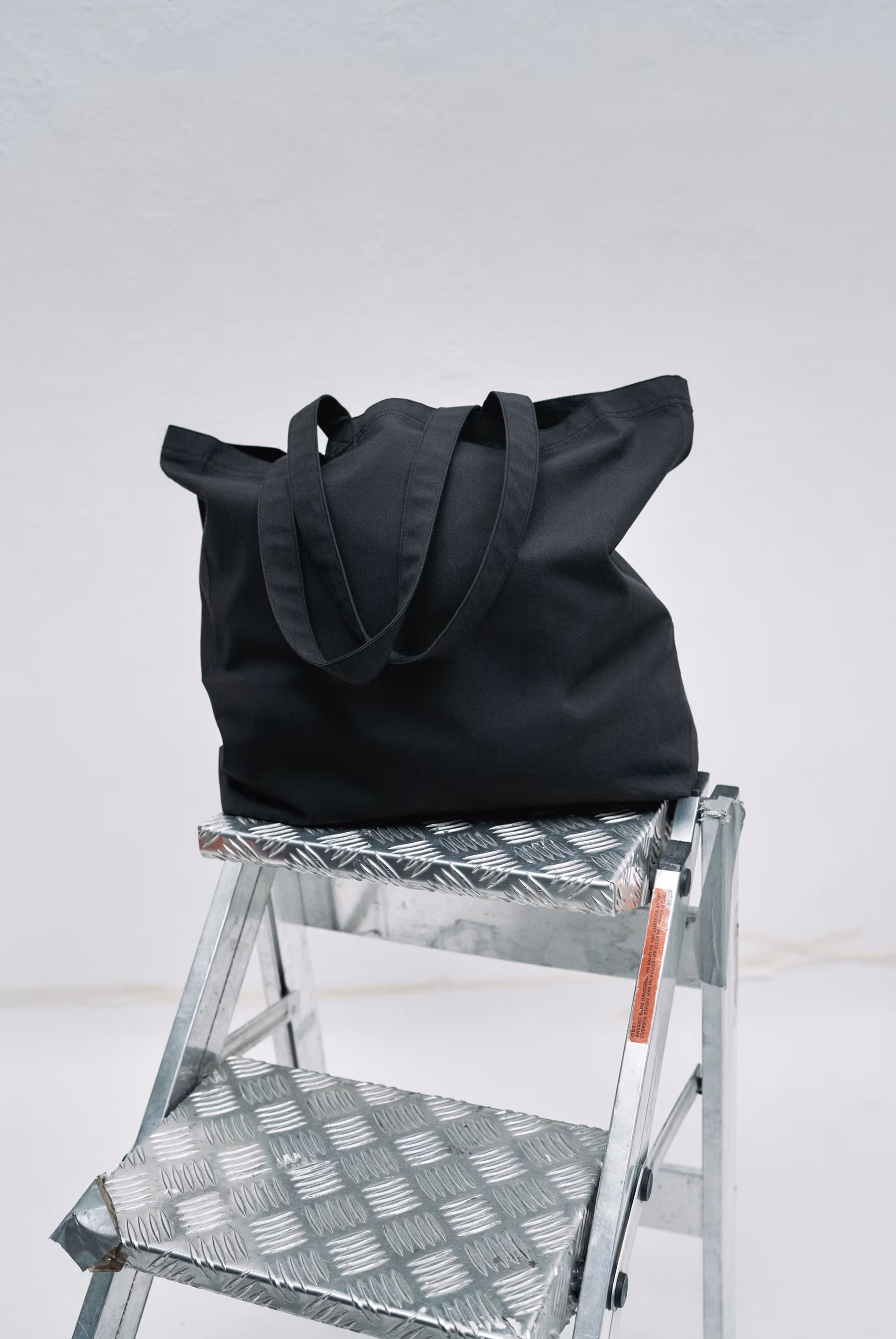A black large tote bag on top of a ladder