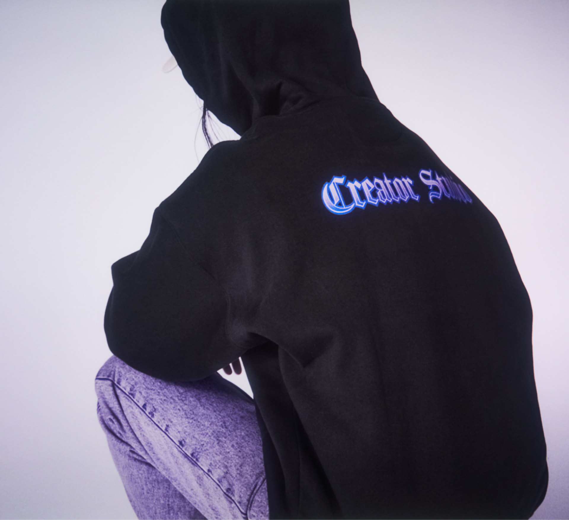 A model wearing a black hoodie with Creator Studio back print