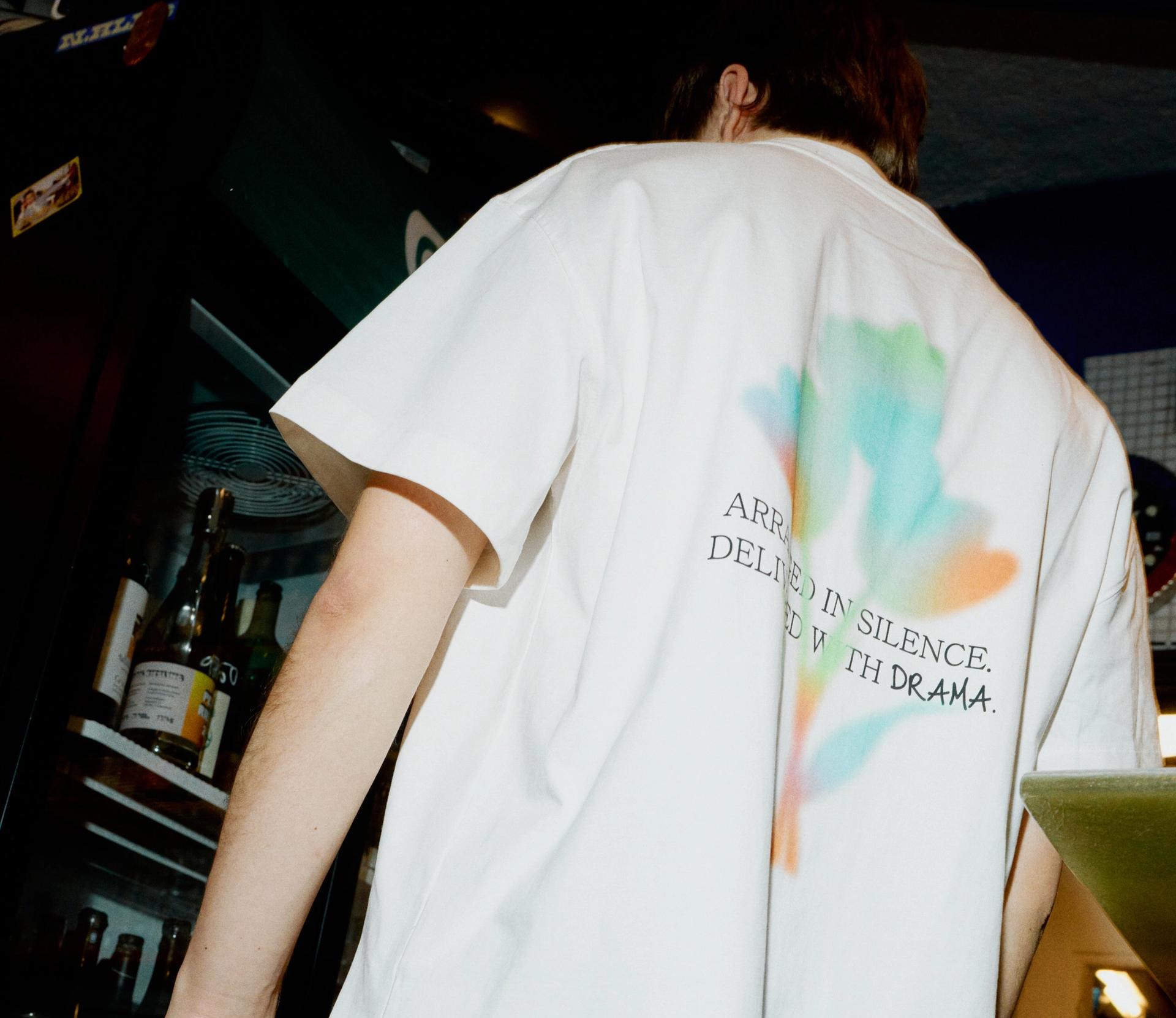 A male model wearing a custom white tee with colourful back print