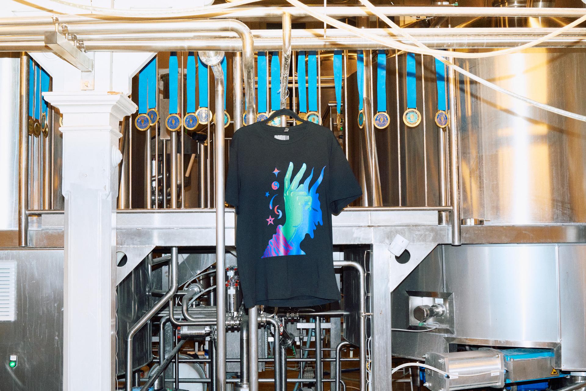 A black T-shirt with a print and a background of a beer brewery place.