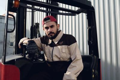 A forklift operator in a cap seated at the controls, looking at the camera