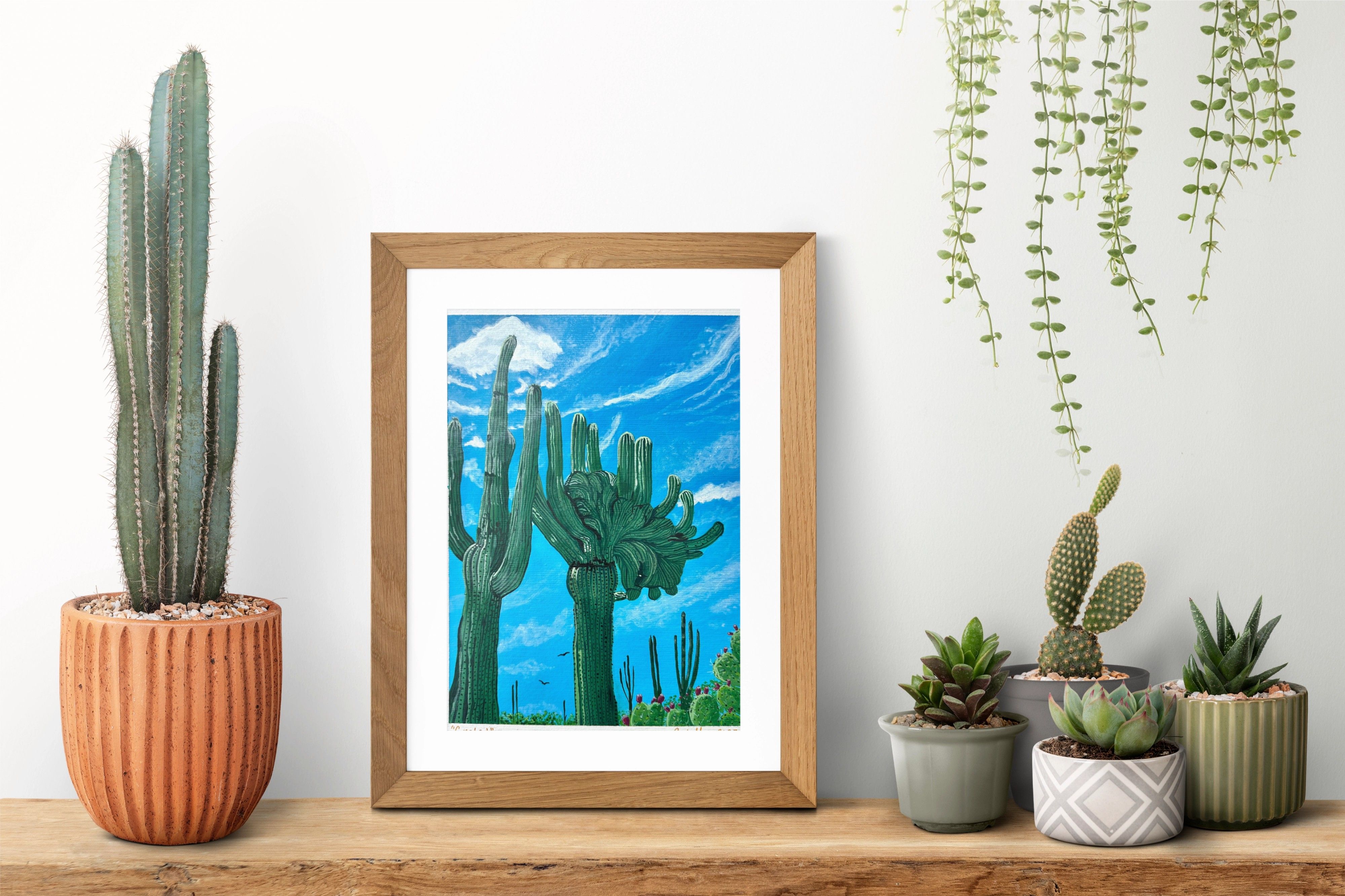 Original Painting of a two saguaro cacti. One is beautifully crested. The sky behind them is a beautiful blue with other desert life in the background.
