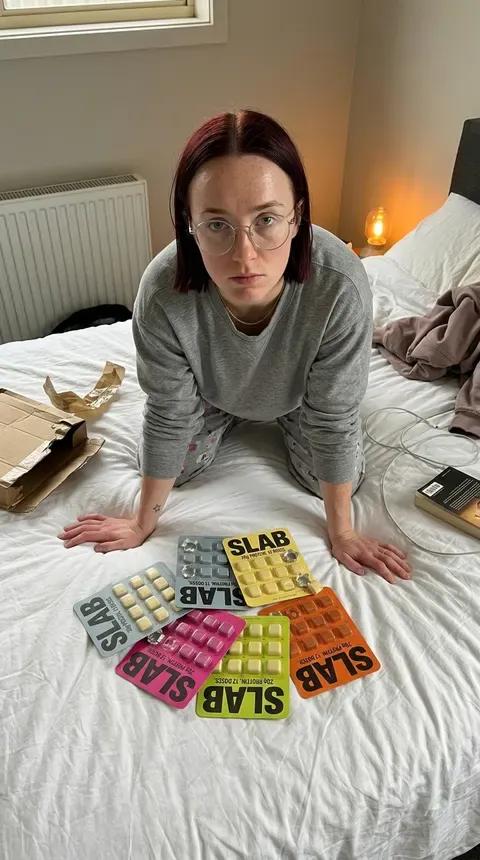 A woman kneeling on an unmade bed surrounded by SLAB trays in six different colourways, spelling the name across the duvet.