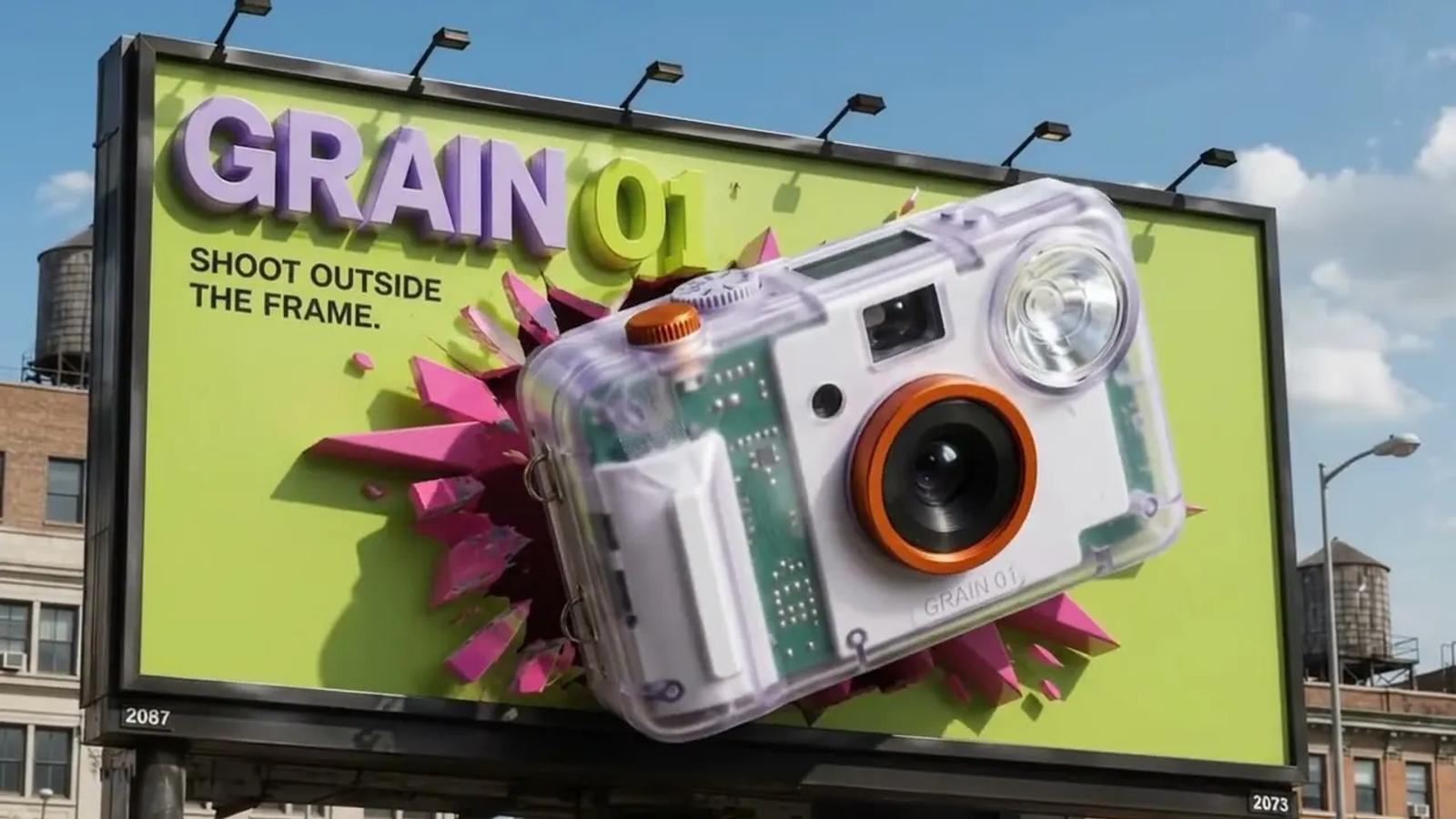 A daylight city billboard for GRAIN 01 on an acid-green ground, the translucent camera bursting through the board in a spray of magenta shards under the line SHOOT OUTSIDE THE FRAME.