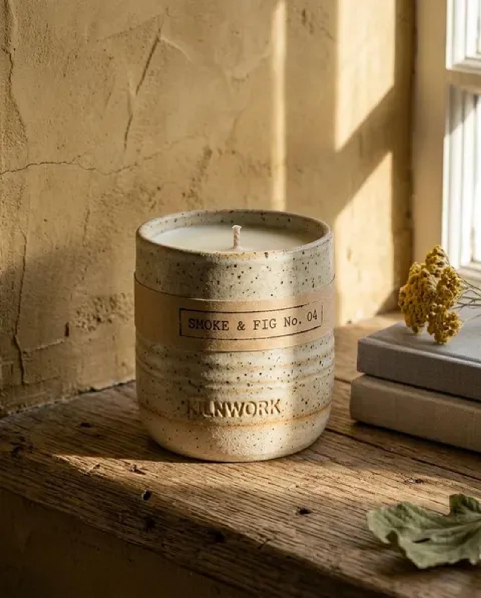 The same candle on a weathered wooden window shelf in warm afternoon light, unlit, a stack of books and a dried flower behind it.