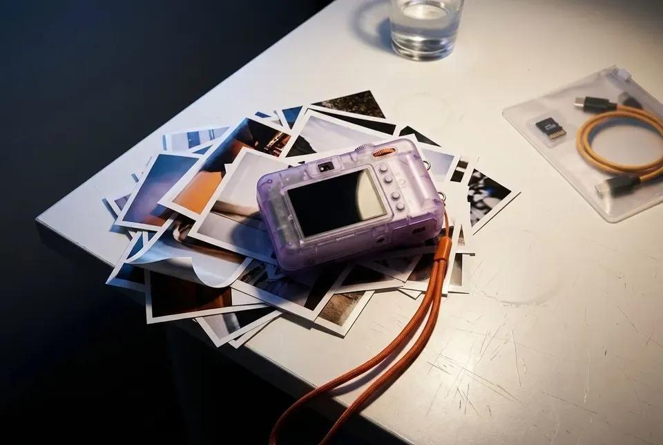 The GRAIN 01 lying on a scattered pile of its own prints and a coiled orange wrist strap on a pale desk.