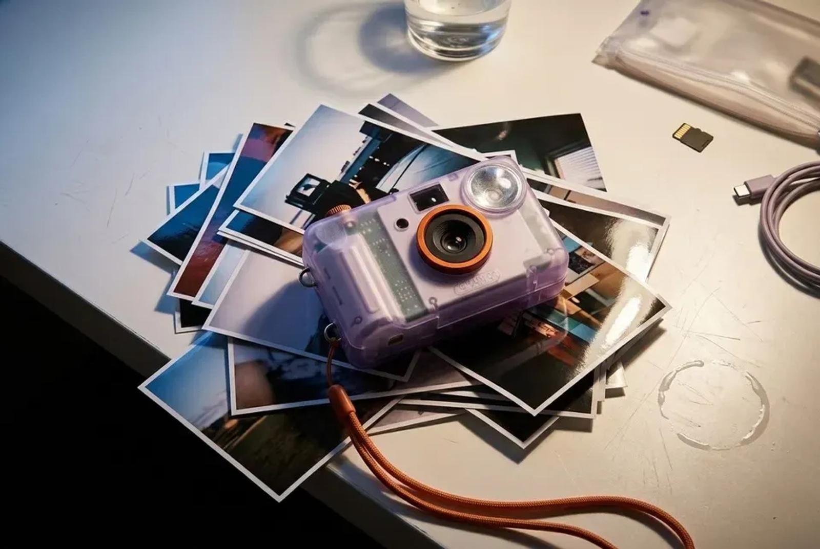 The same pile of prints and the camera shot from a lower angle, a memory card and a glass of water at the edge of frame.