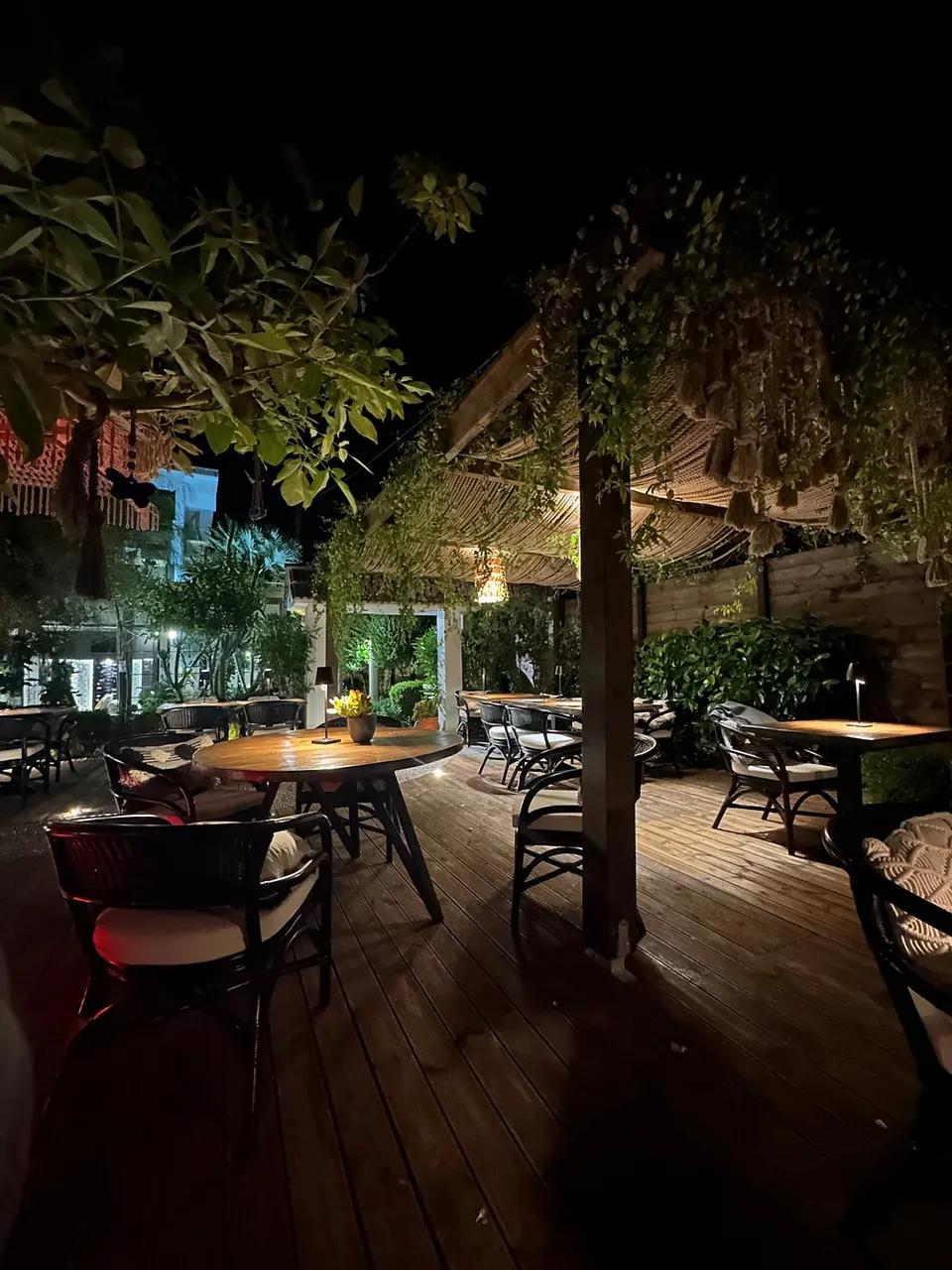 The terrace at Mariposa after dark, wooden decking, cane shades, planting overhead and a lit table in the middle distance.
