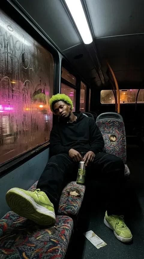 The same man sprawled across a night tram seat with a FERAL can between his feet, neon strip lighting down the carriage behind him.