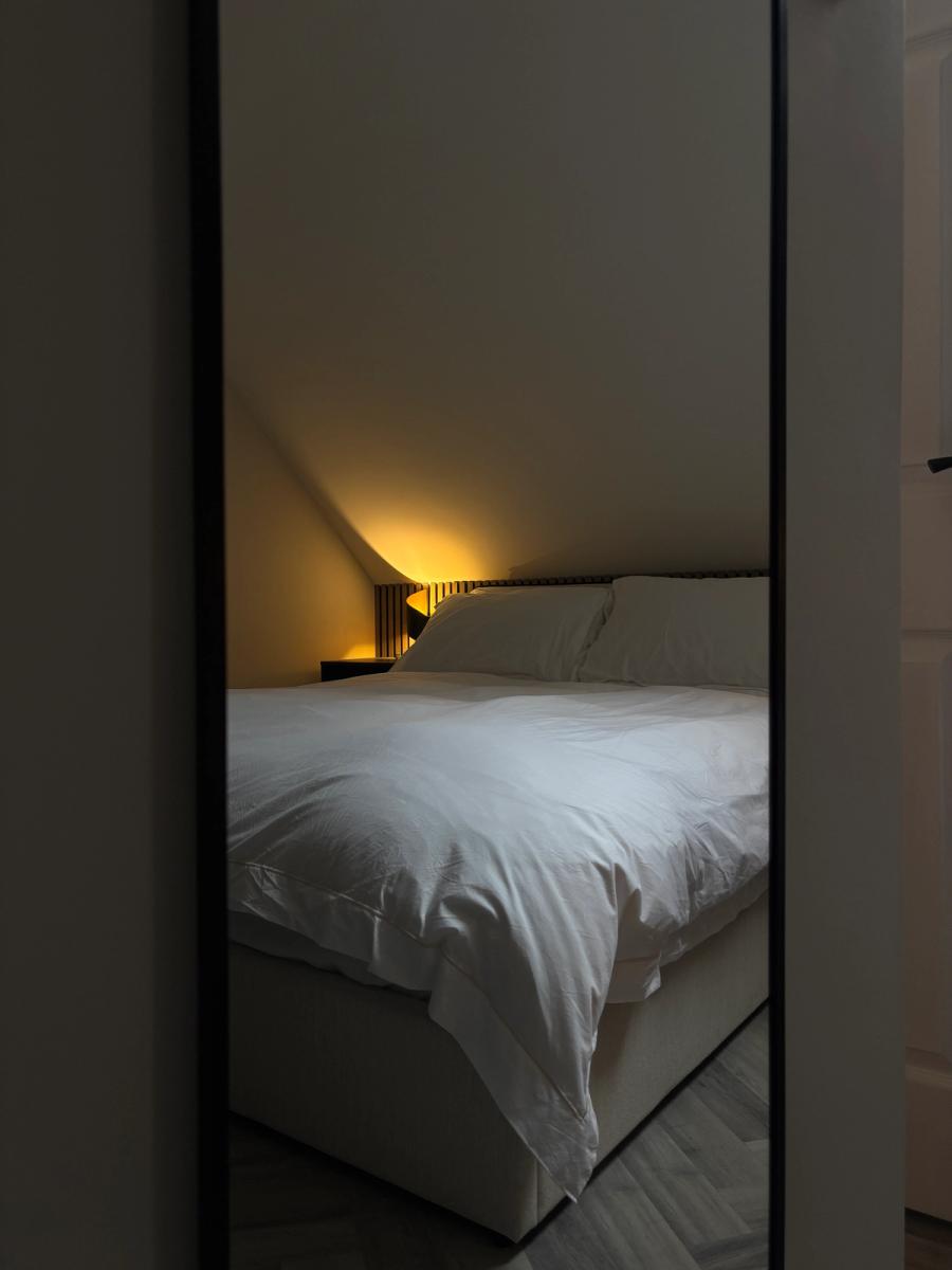 The loft bedroom reflected in a full-length mirror, herringbone flooring below the sloped ceiling.