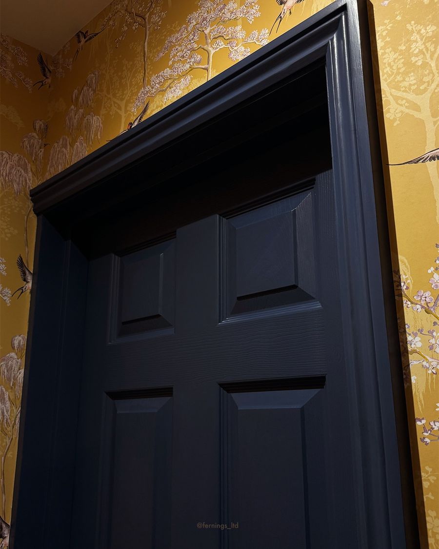 A deep navy panelled door set against golden bird-print wallpaper.