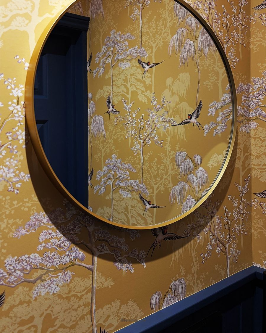 A brass-framed round mirror on the golden bird-print wallpaper of the new cloakroom.