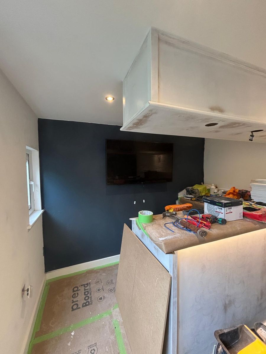 The media wall in its first coat of deep navy, floors still under protection boards.
