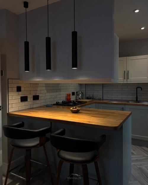 The refurbished kitchen in Ashtead: sage cabinetry, solid oak worktops and black pendant lights over the breakfast bar.