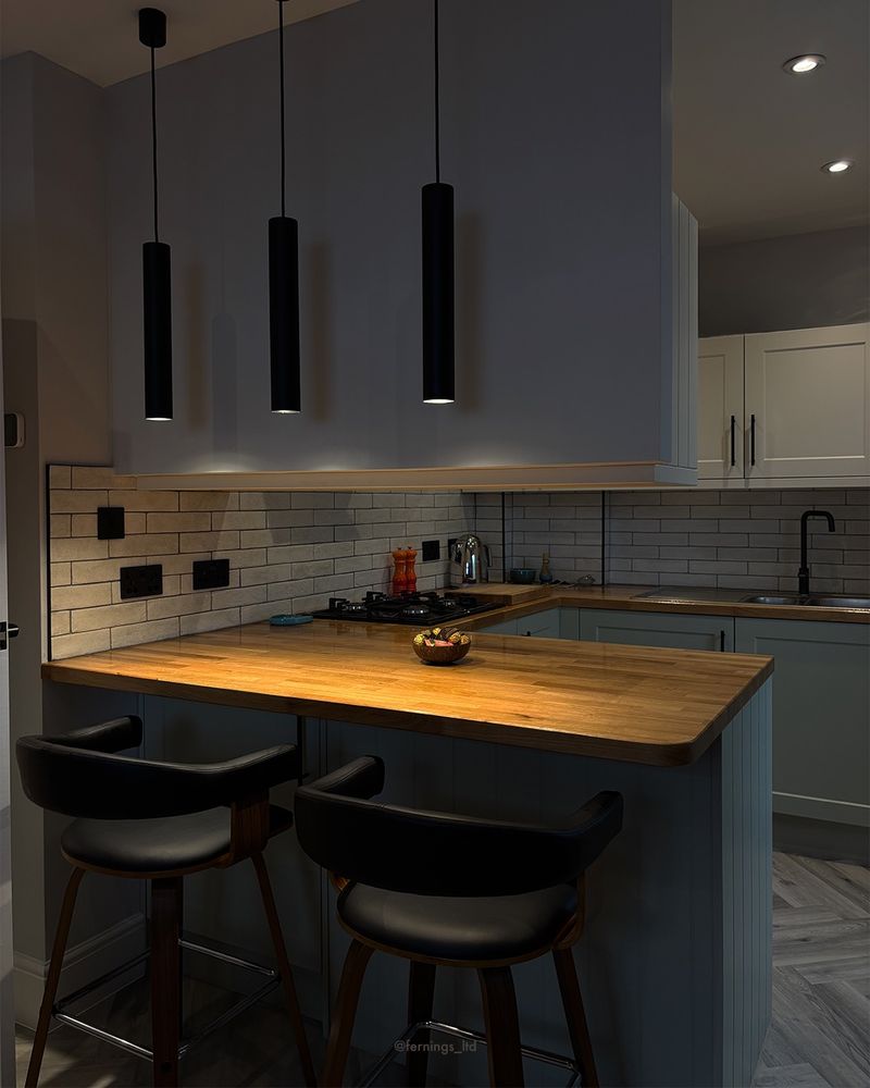 The refurbished kitchen in Ashtead: sage cabinetry, solid oak worktops and black pendant lights over the breakfast bar.