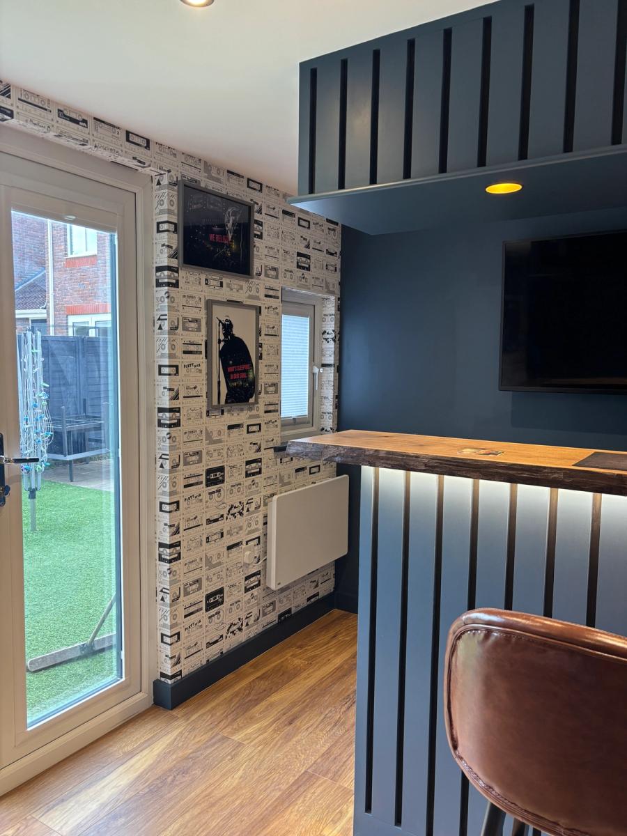 The live-edge walnut counter, under-lit bar front and slatted media wall, looking out to the garden.
