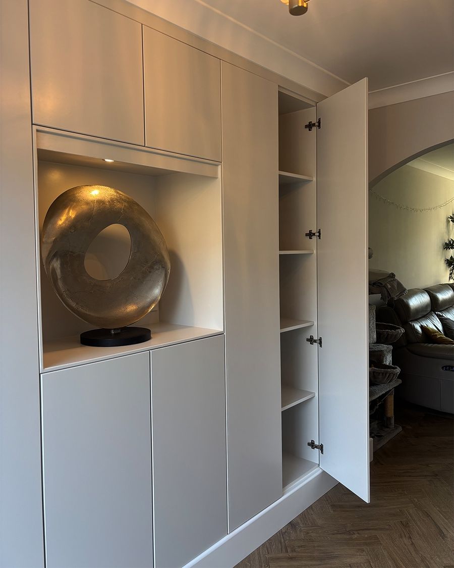 The fitted cupboards with their lit display niche, one door open to the shelving inside.
