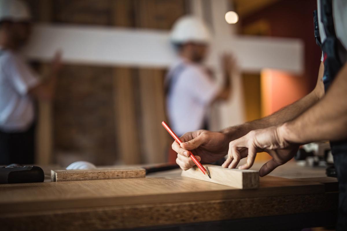 On site during a residential build, a carpenter marks timber by hand as the team works in the background.