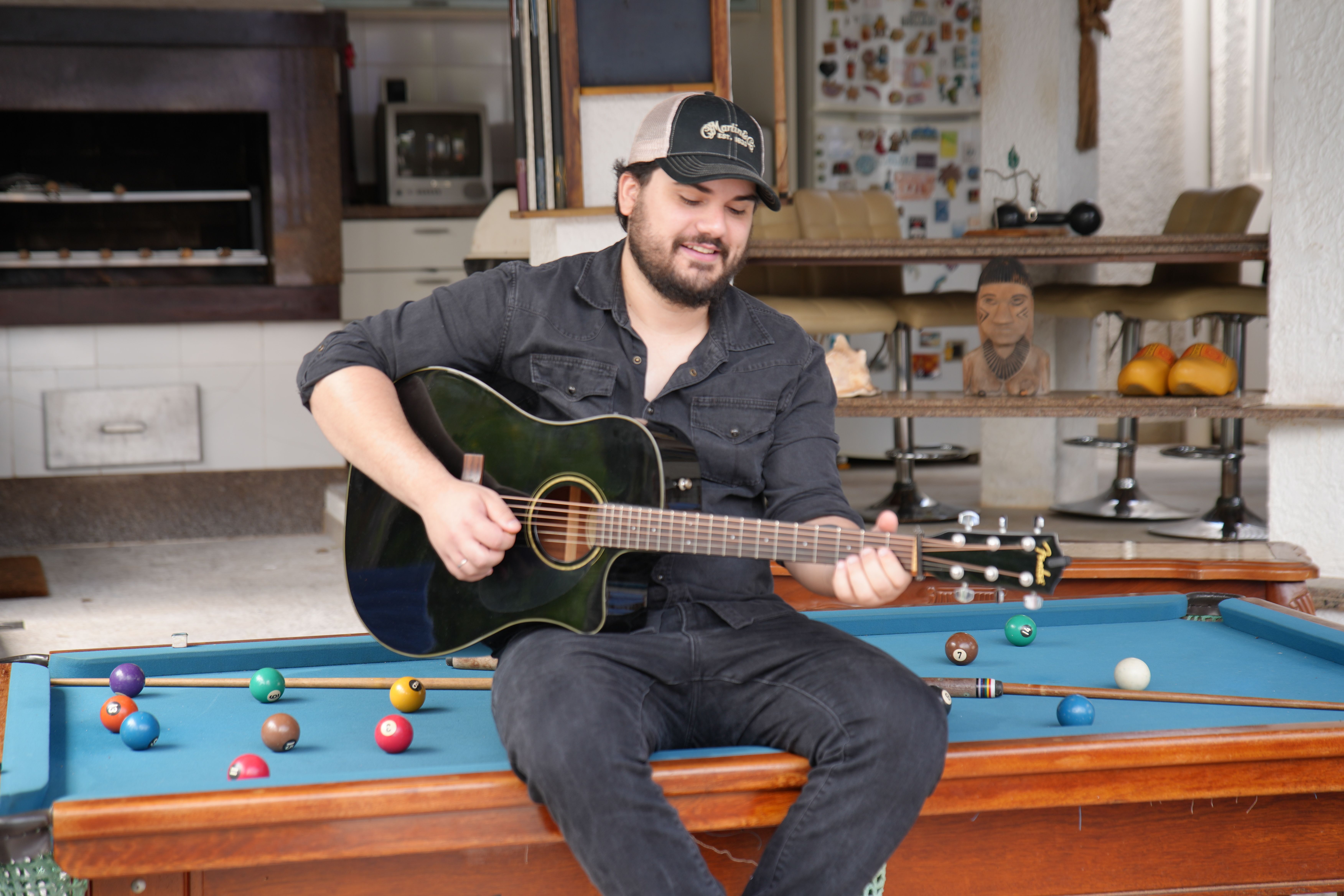Matheus Granjeiro na mesa de sinuca, olhando para o violão