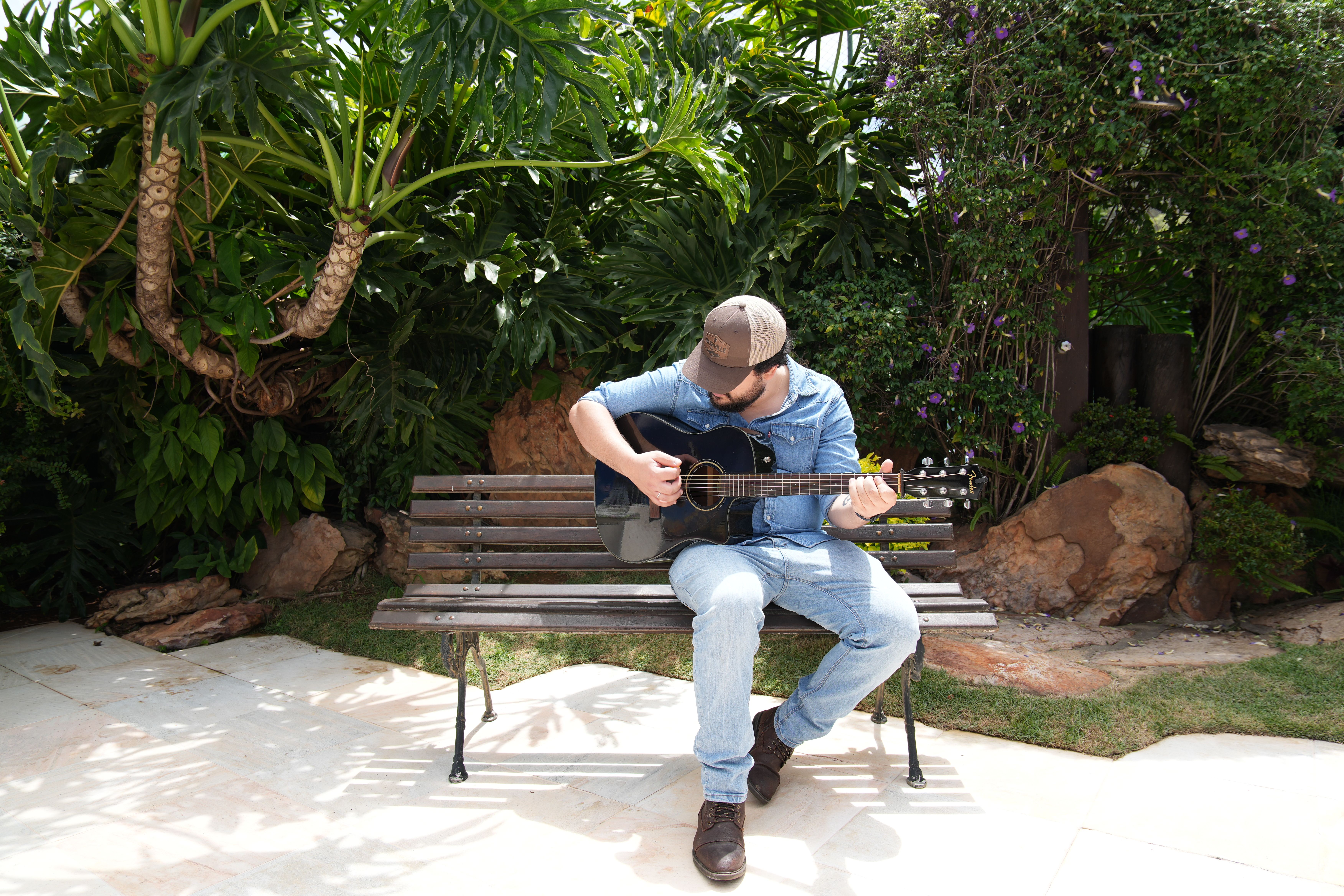 Matheus Granjeiro tocando violão no jardim, visto de lado