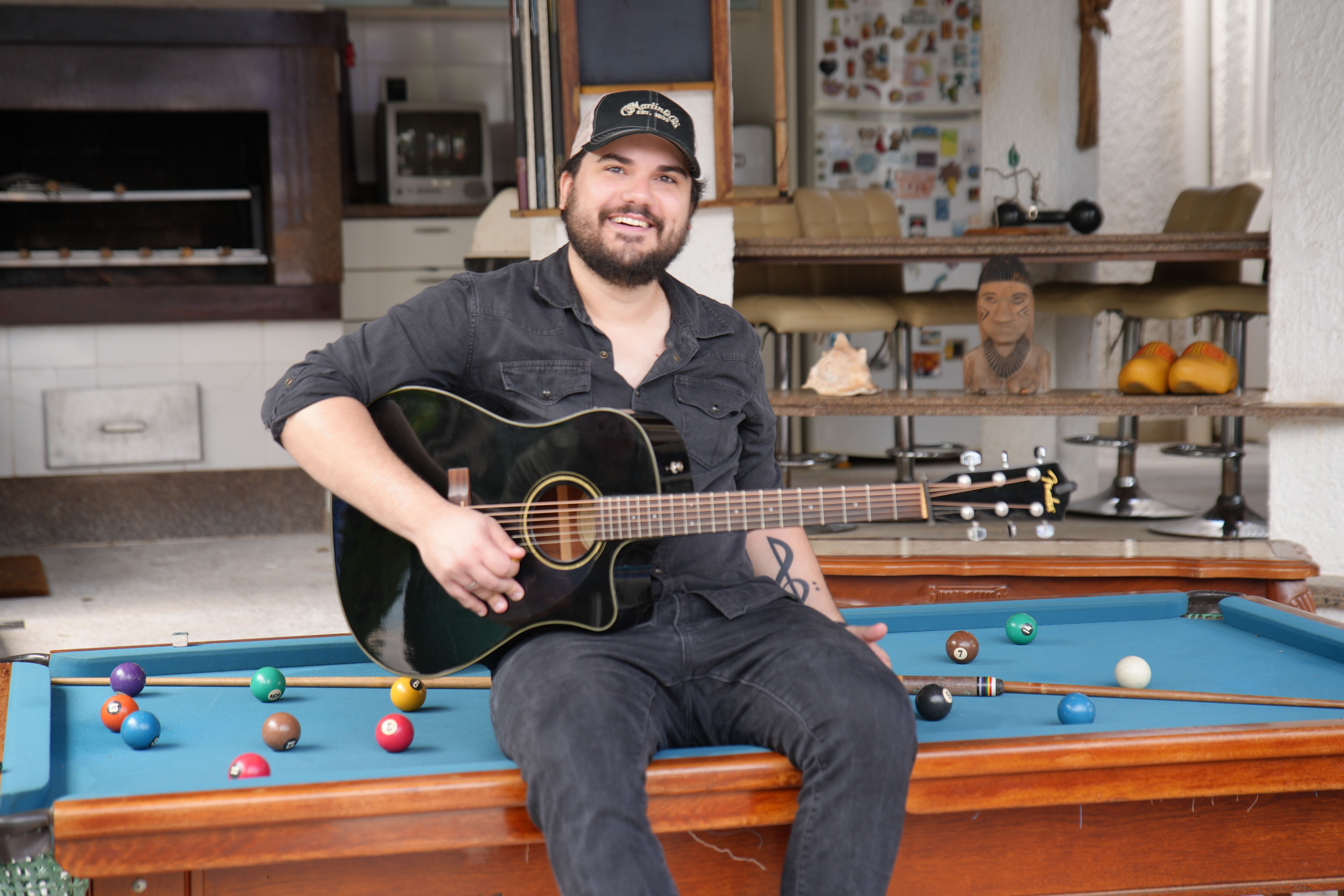 Matheus Granjeiro sentado na mesa de sinuca com o violão