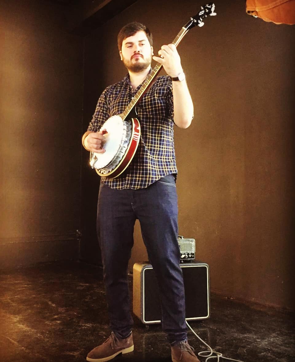 Matheus Granjeiro em pé com um banjo, fundo de estúdio
