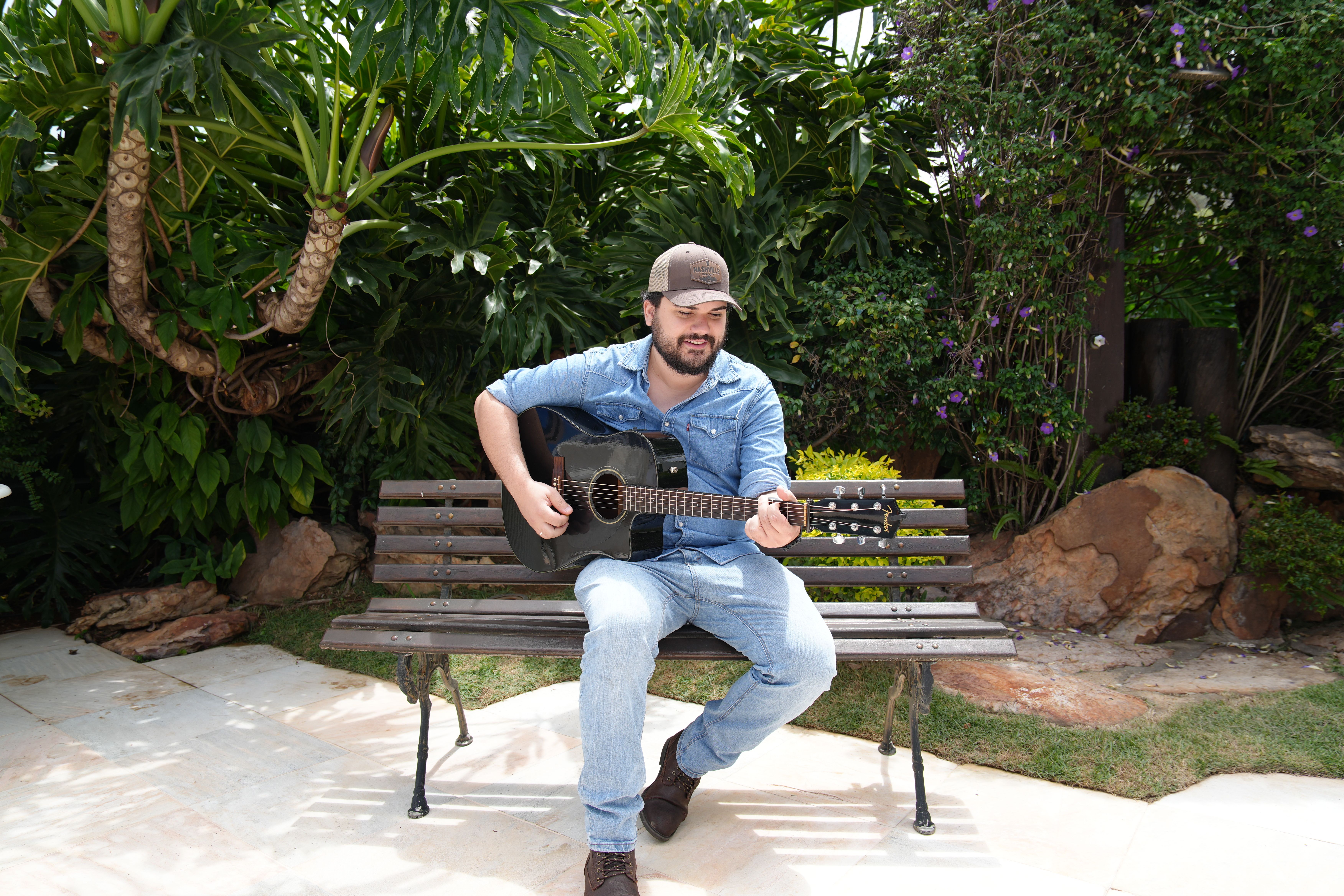 Matheus Granjeiro tocando violão em um banco de jardim